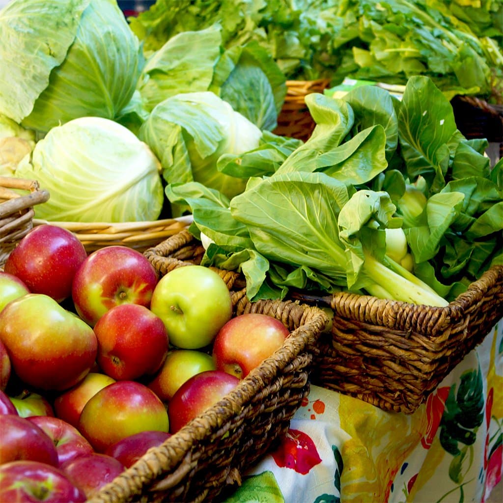 Photo of red and green apples and leafy greens in baskets on a table for a free farm stand in Harlem, NYC.