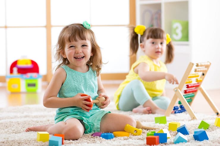 Toddlers playing with colorful toys and blocks in a bright classroom.