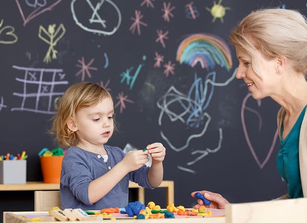 Young child creating with hands on materials beside a teacher at Great Beginnings Preschool in Goodyear AZ