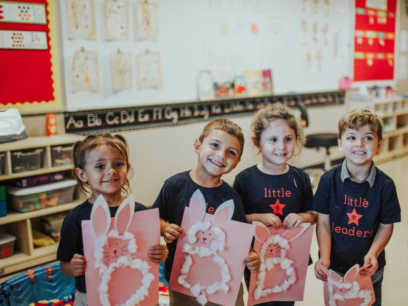 Four Little Leaders students happily holding up their artwork in the front of class