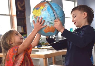 Two children holding and exploring a globe indoors.