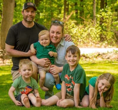 A happy family of six posing together outdoors in a green park.