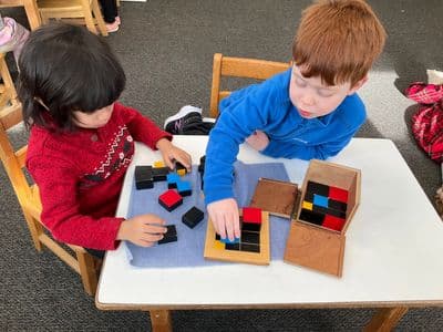 Two children playing with colorful wooden blocks at a table.
