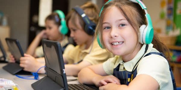 Children using tablets with headphones in a classroom.