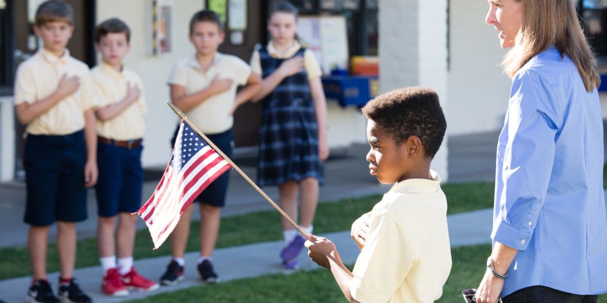 Children pledging allegiance to the American flag with teacher.