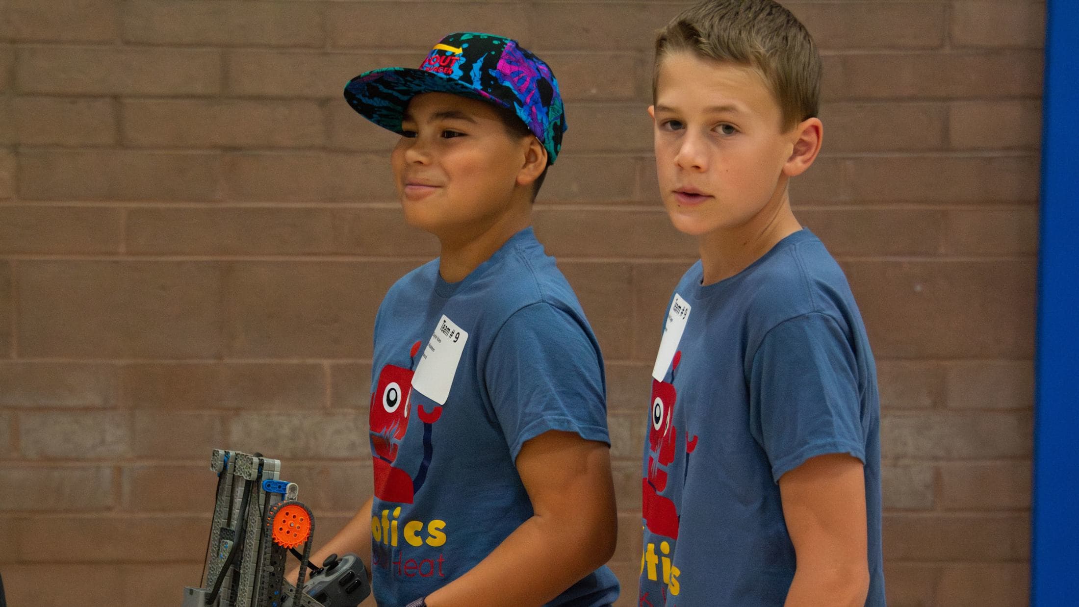 Two young boys wearing matching blue shirts with graphics on them, standing in front of a brick wall.