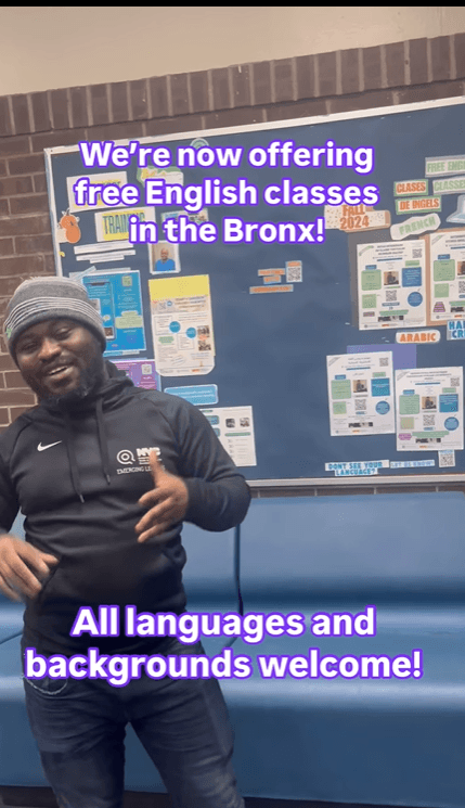 A person in a black hoodie stands in front of a bulletin board with various posters, promoting free English classes in the Bronx, welcoming all languages and backgrounds.