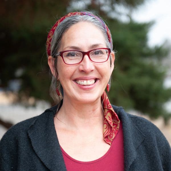 Smiling woman wearing red glasses and a patterned headscarf outdoors.