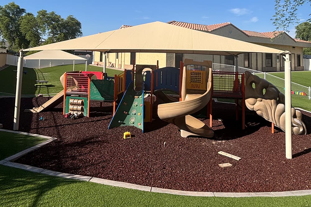 Shaded playground with slides, climbing wall, and tunnels.