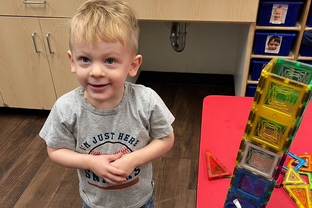 Smiling boy builds a tall tower with magnetic tiles.