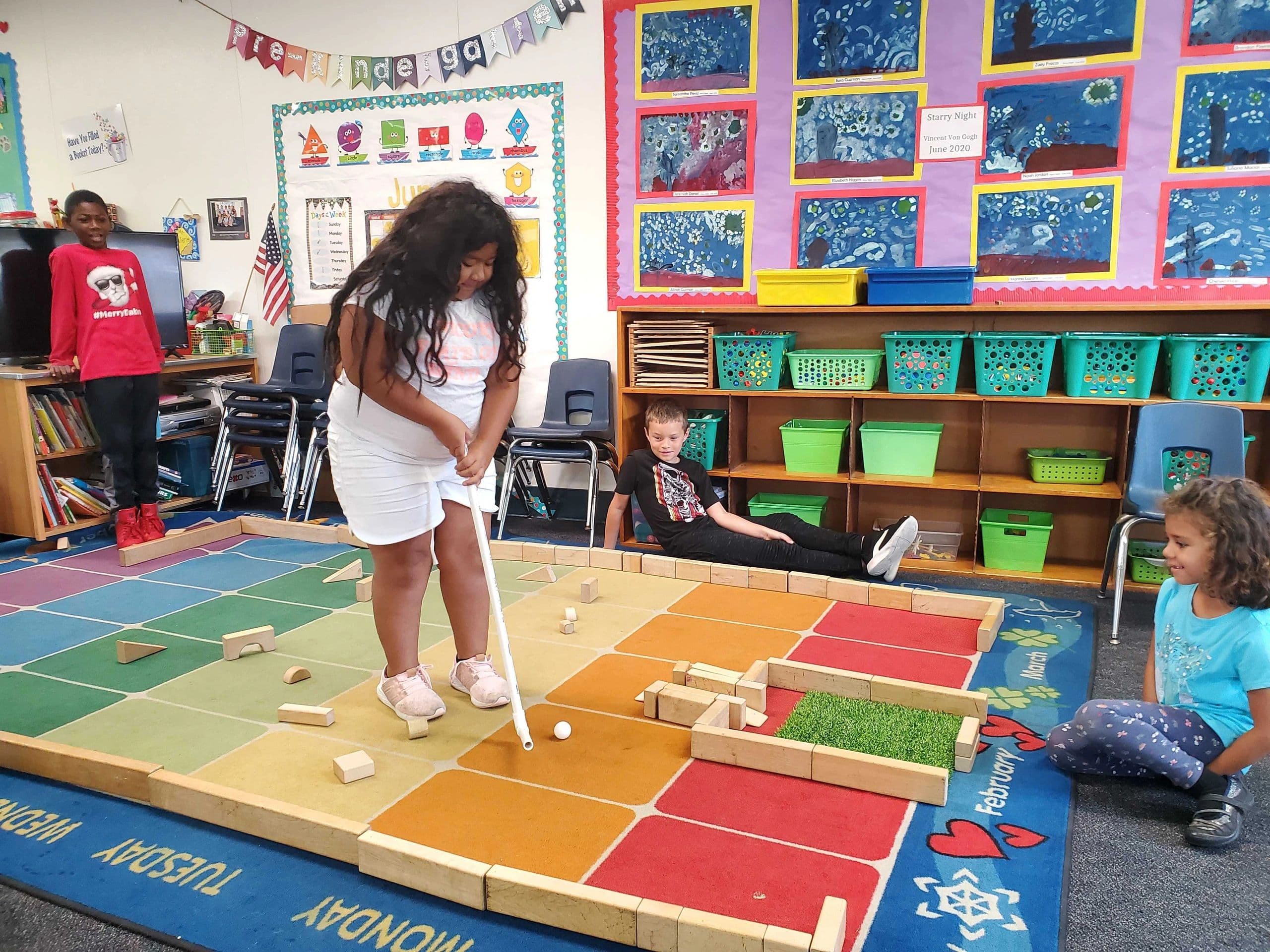 Children playing indoor mini golf in a colorful classroom.