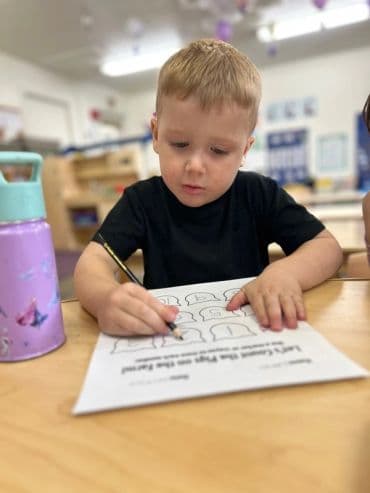 Young boy focused on coloring a worksheet at a classroom table.