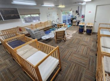 Empty nursery room with wooden cribs and play area.