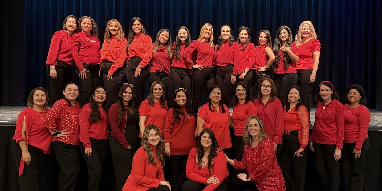 Group of women dressed in red tops and black pants posing on stage.