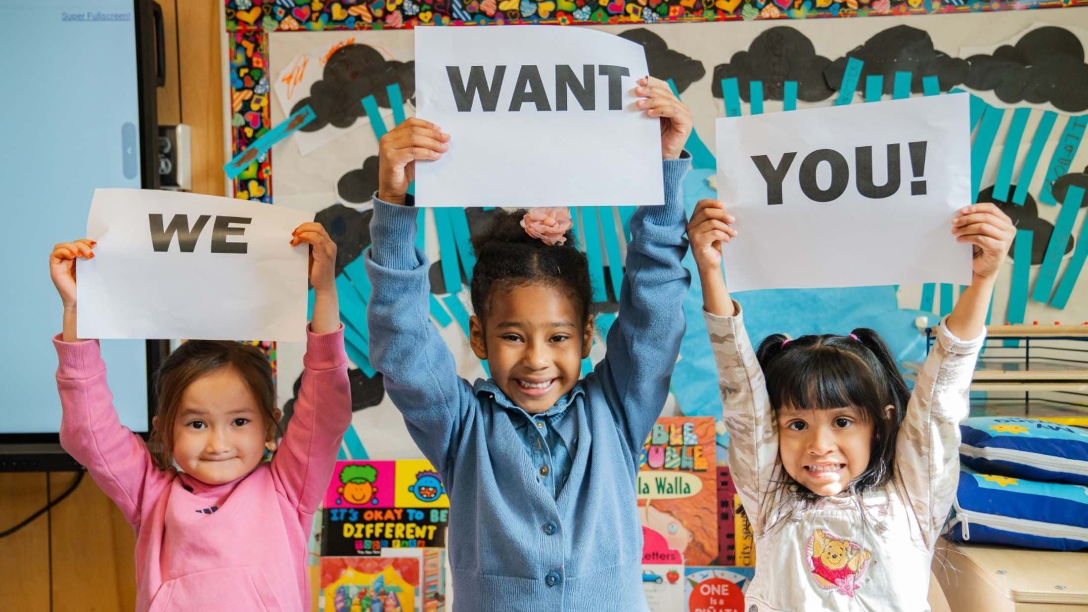 Young students holding signs that read We Want You