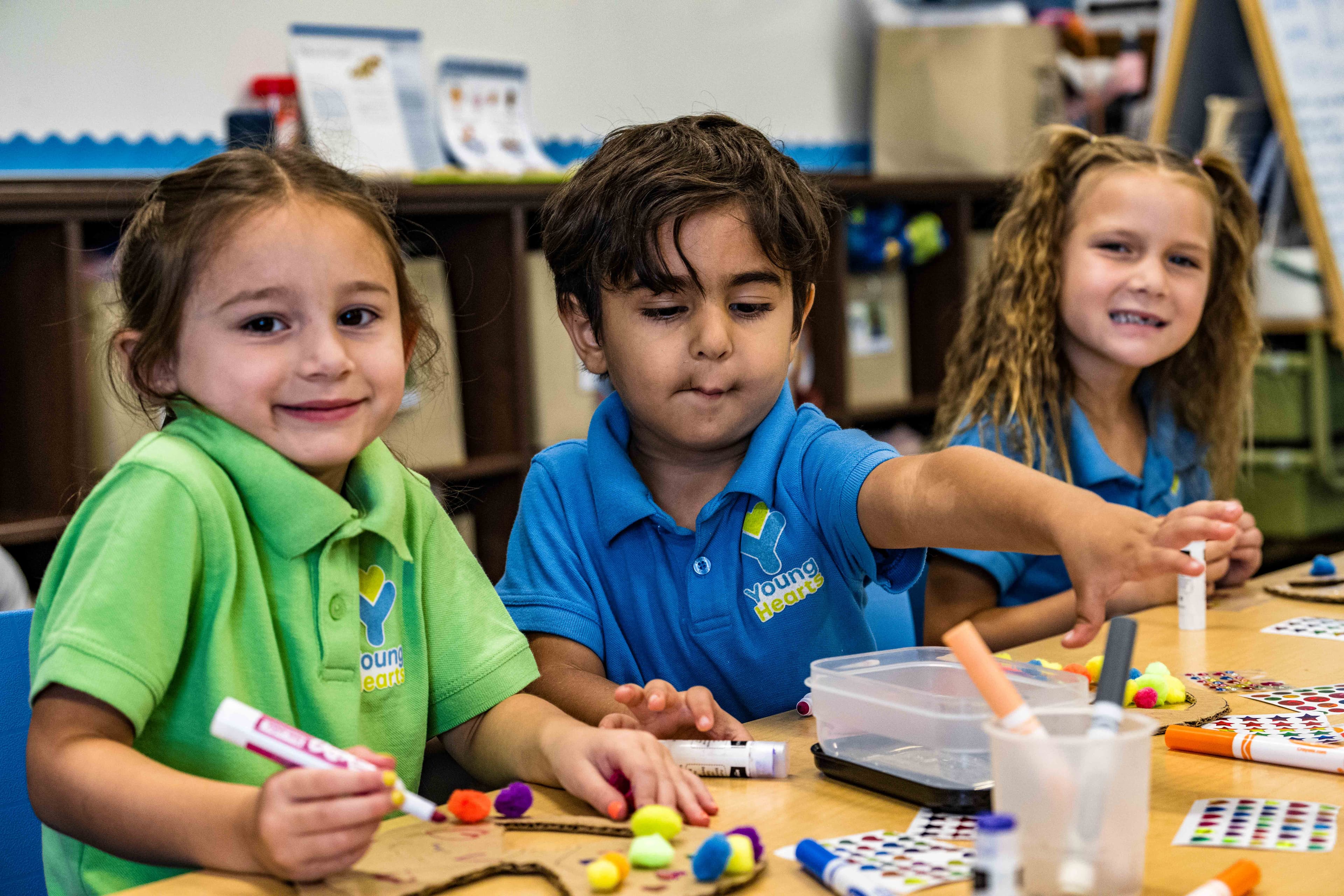 Three preschool students sitting at a table working on art projects