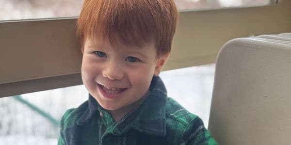 Smiling young boy with red hair wearing a green plaid shirt.