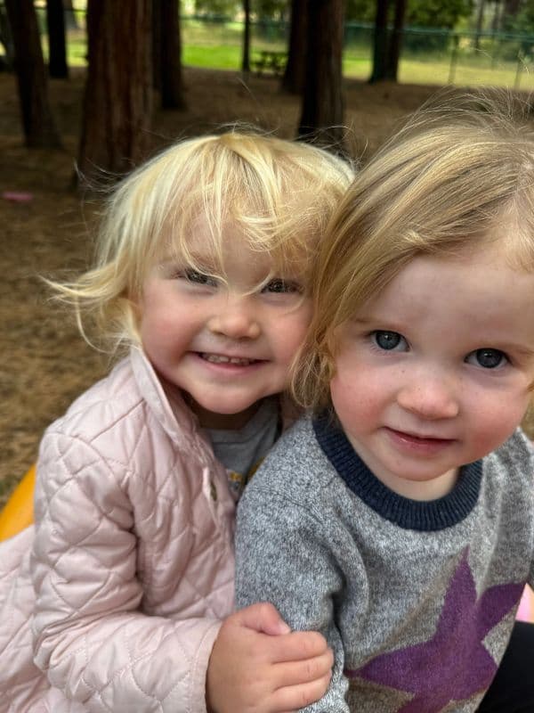 Two young children hugging and smiling outdoors.