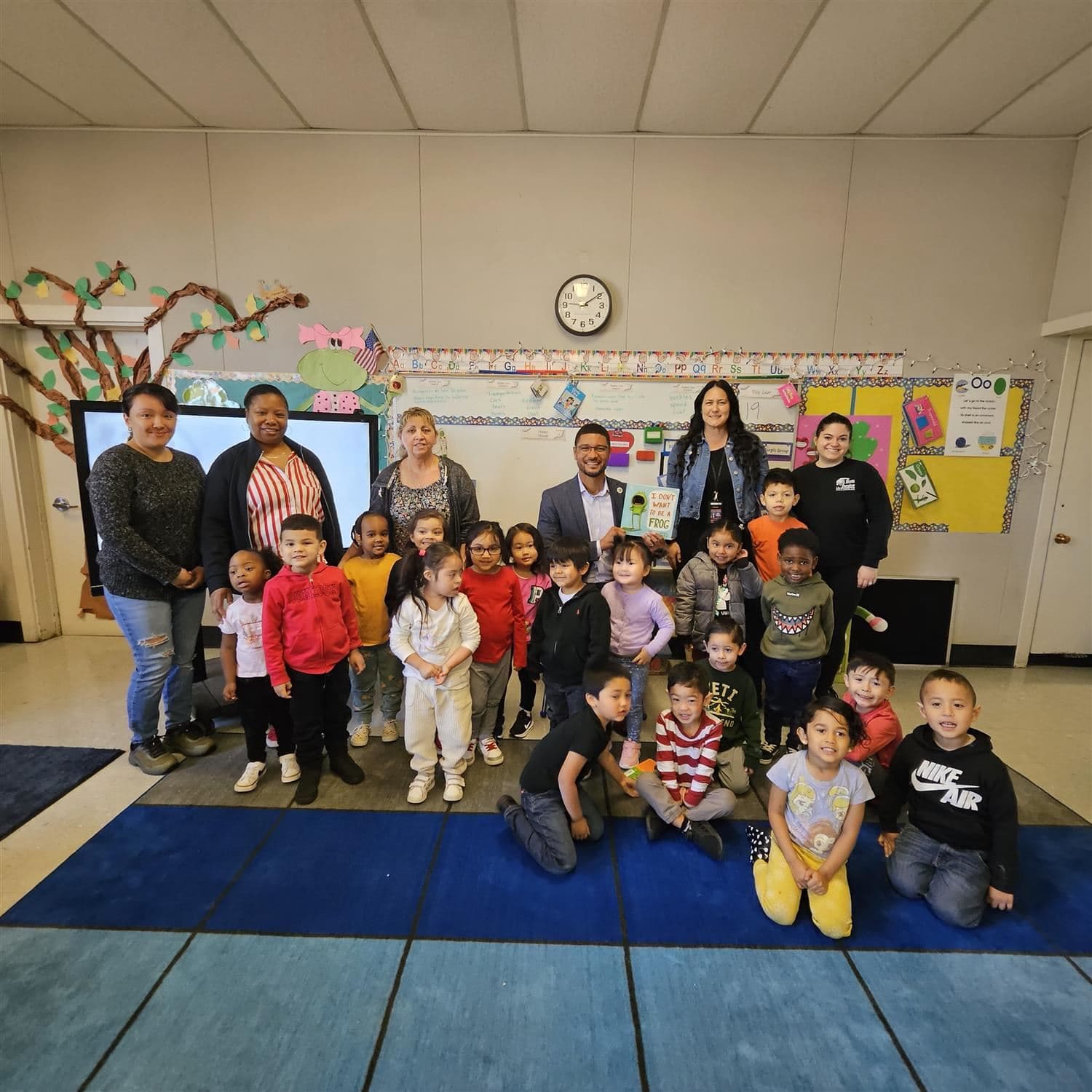 A group of children and adults pose together in a brightly lit classroom.