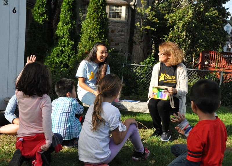 Group of kids with 2 aids having circle time outside