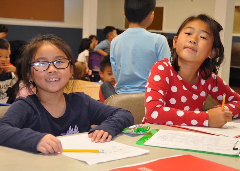 2 elementary schools students working on homework and smiling