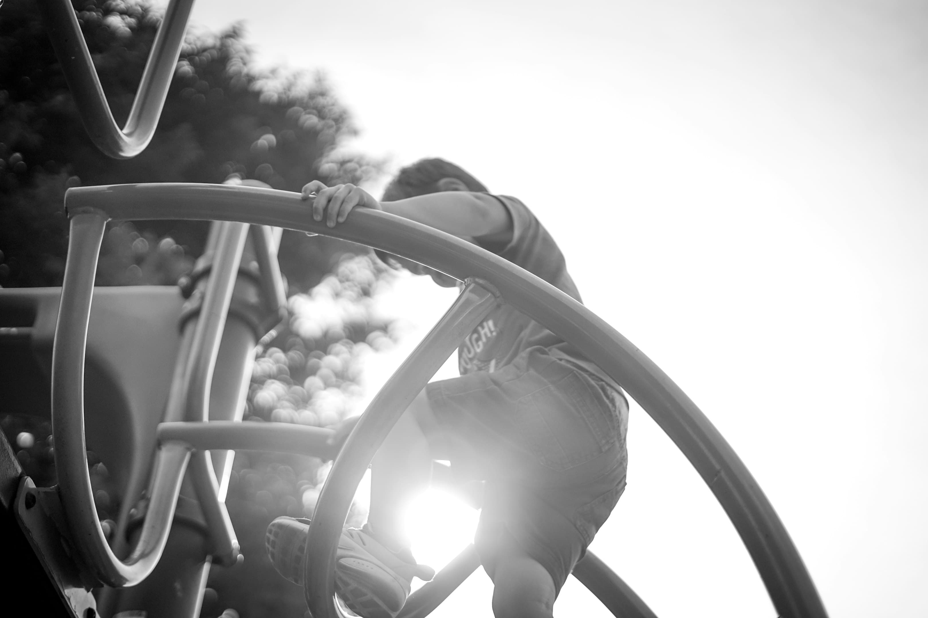Child climbing on playground equipment with sun shining in the background.