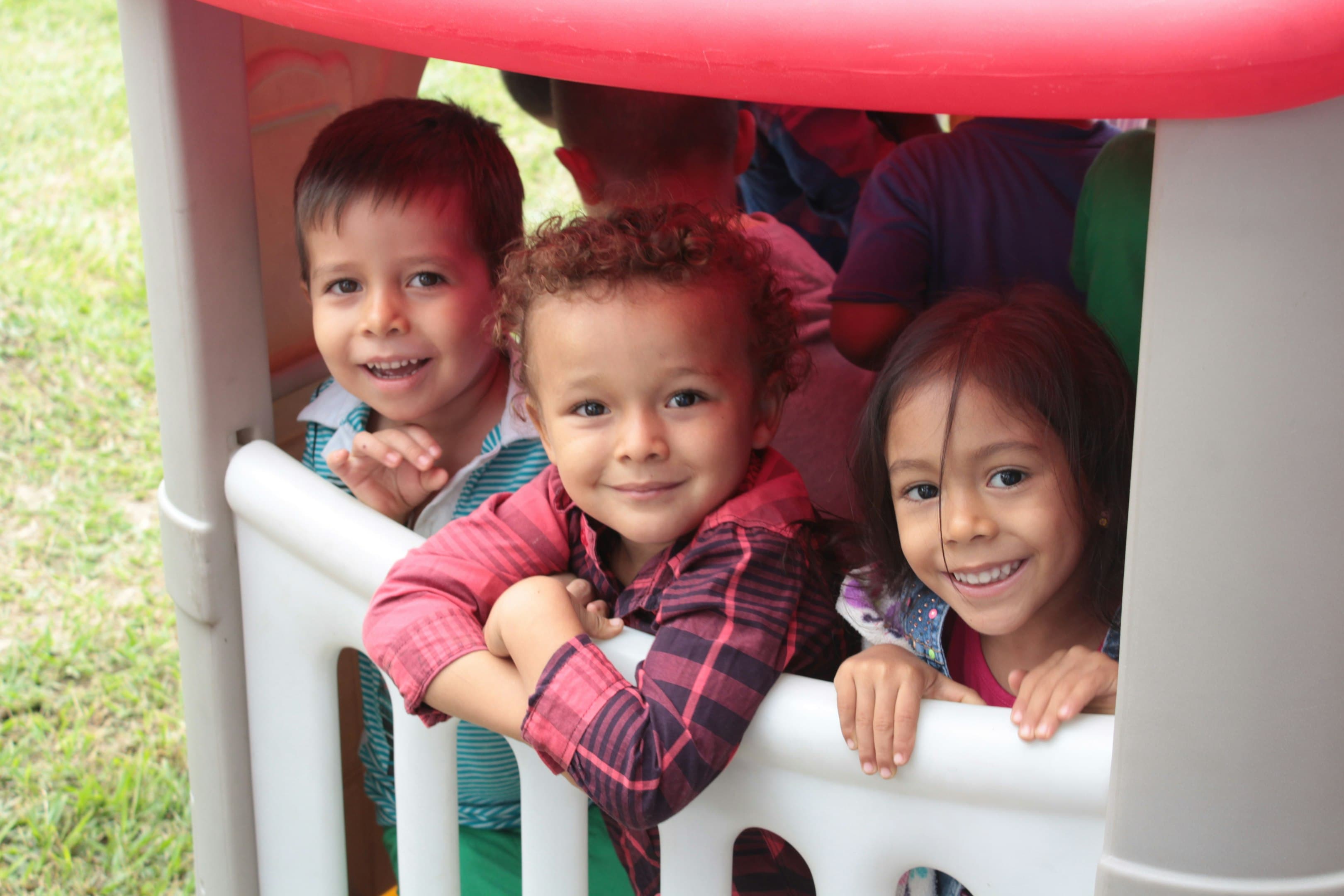 Three smiling children playing in a playground structure.