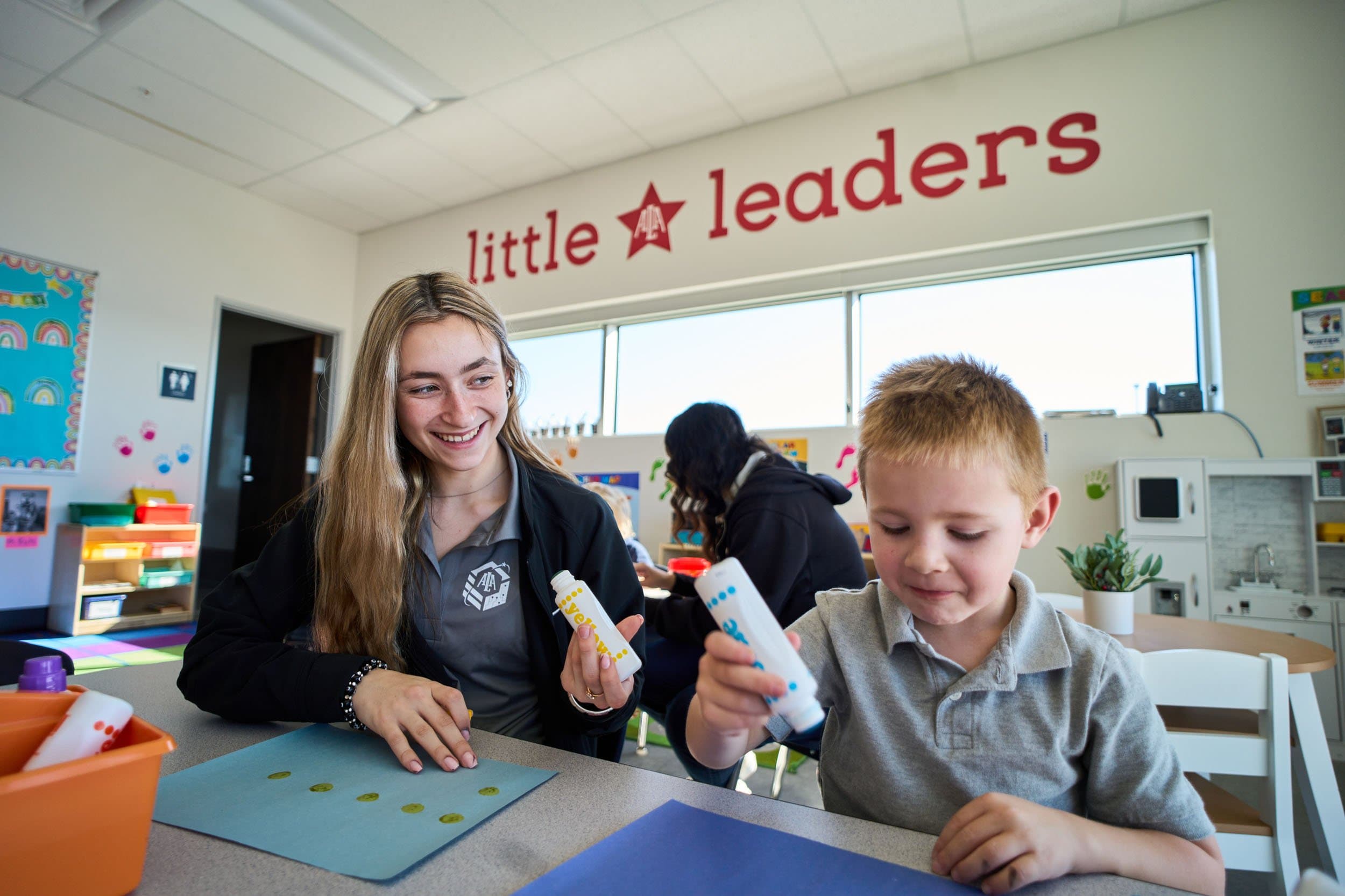 A girl smiling, interacts with a boy who is engaging in craft activities.