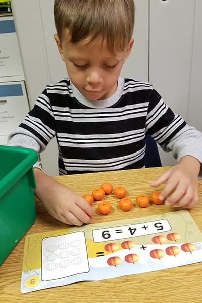 Preschooler uses tiny pumpkins to complete a math problem.