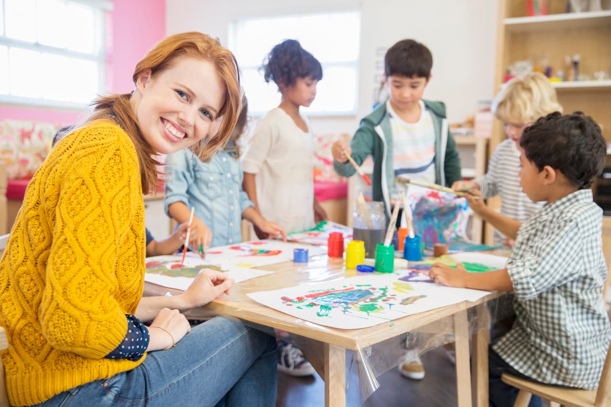 A teacher sitting with students at a table doing activities