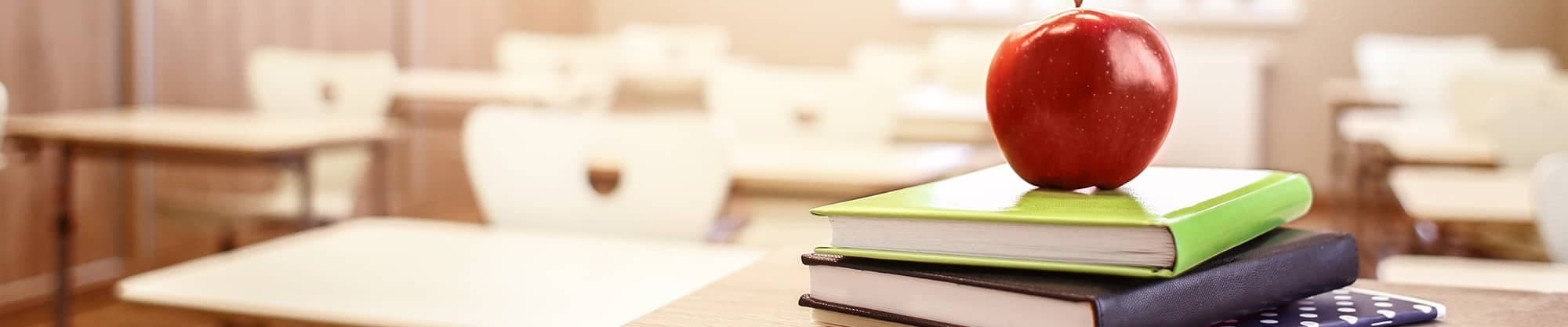 stack of books with apple on desk in classroom
